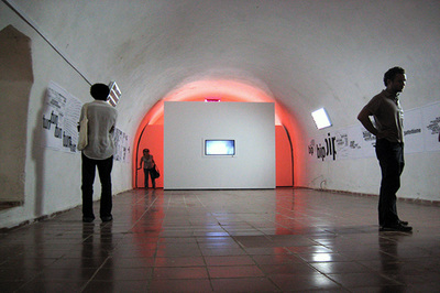 two people standing on open hallway, back wall with a video screen and orange background light